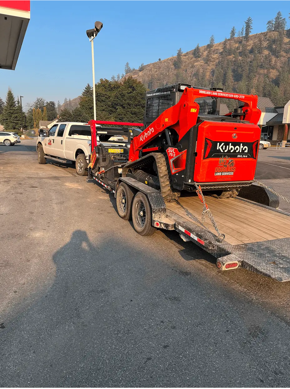 White pickup hauling red Kubota compact loader